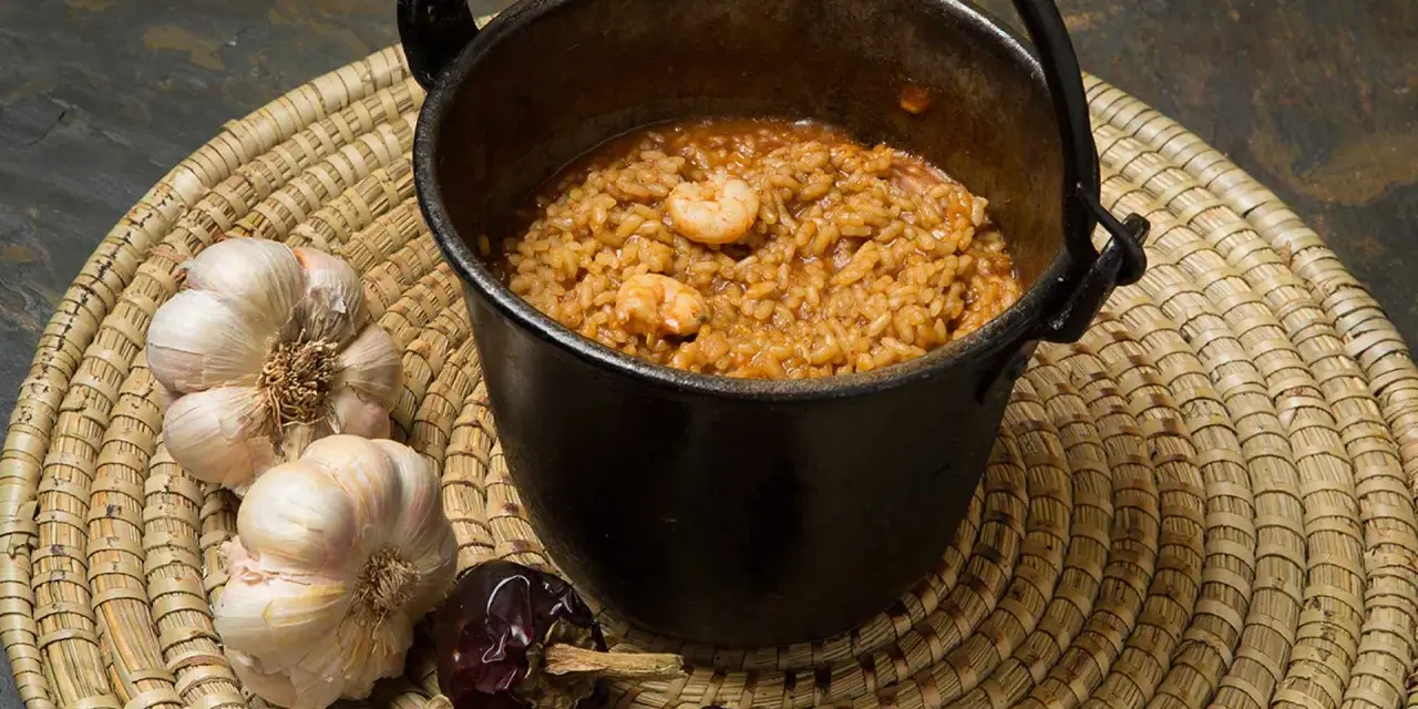 Caldero murciano humeante en olla de hierro, con gambas, ajos y pimientos secos.