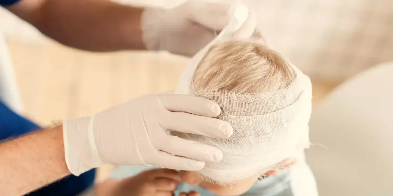 Manos enguantadas vendan la cabeza de un niño, curando sus heridas.