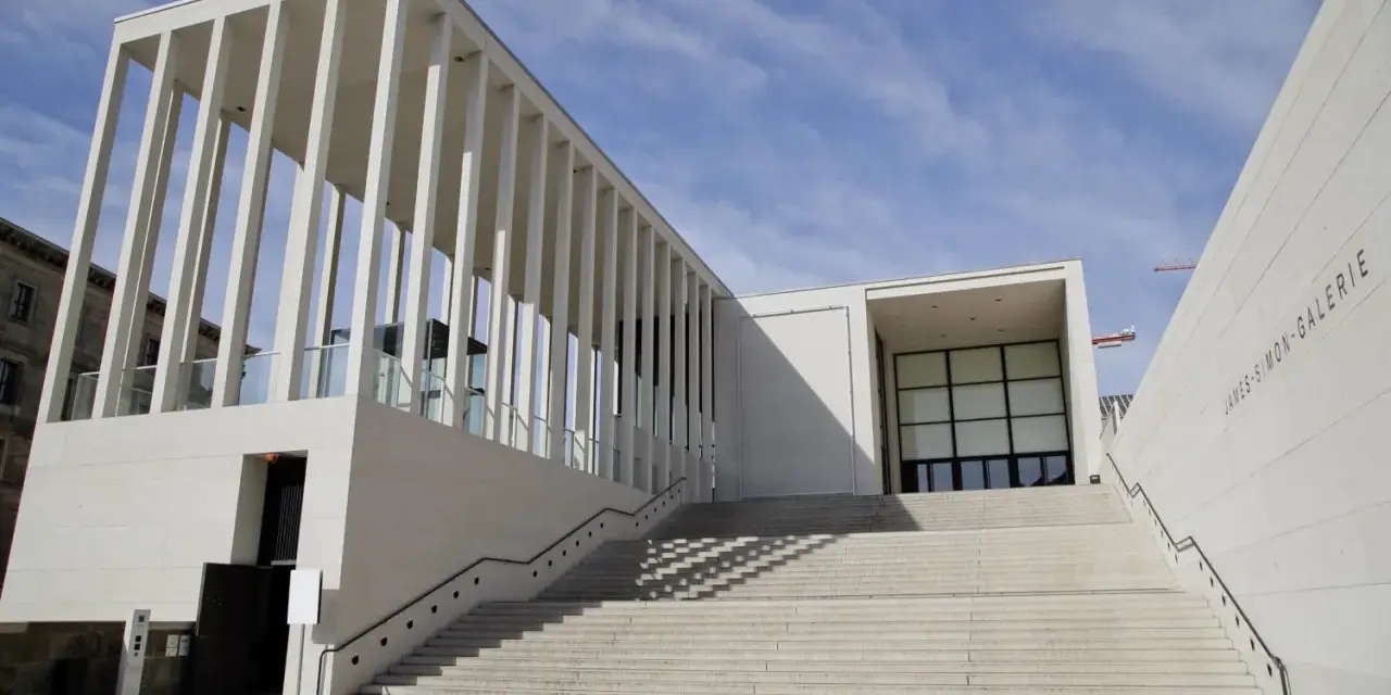 Moderne berlin architektur: James-Simon-Galerie mit langer Treppe und Säulengang vor blauem Himmel.