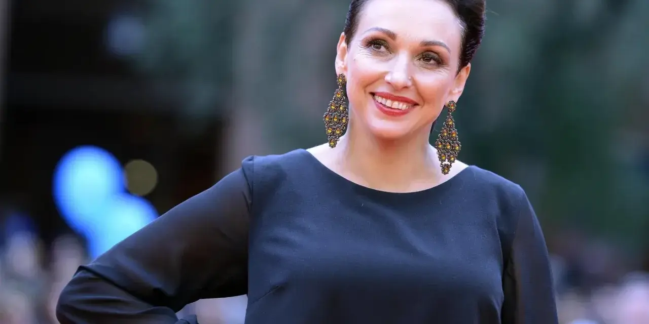 Uśmiechnięta Kinga Dębska w czarnej sukni i ozdobnych kolczykach, pozuje na czerwonym dywanie.