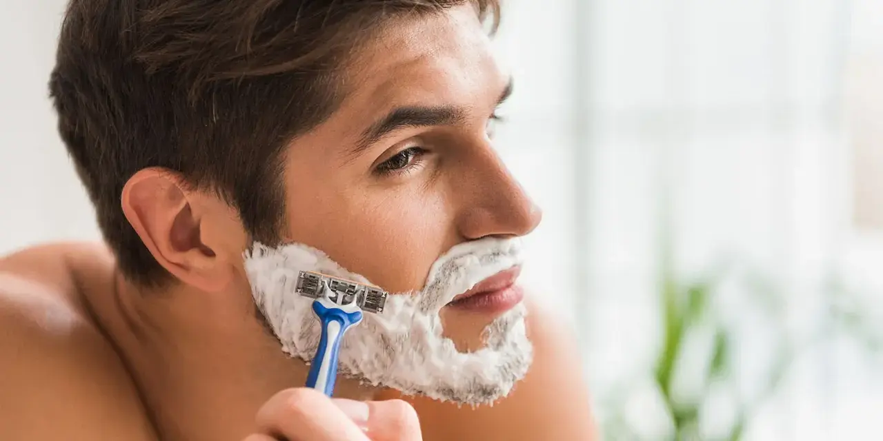 Hombre afeitándose la barba con espuma y maquinilla. La espuma de afeitar sirve para lubricar y proteger la piel.