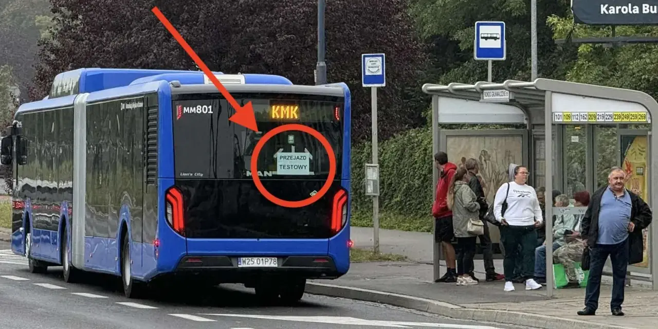 Niebieski autobus przegubowy z napisem "PRZEJAZD TESTOWY" na tyle, stoi przy przystanku autobusowym.