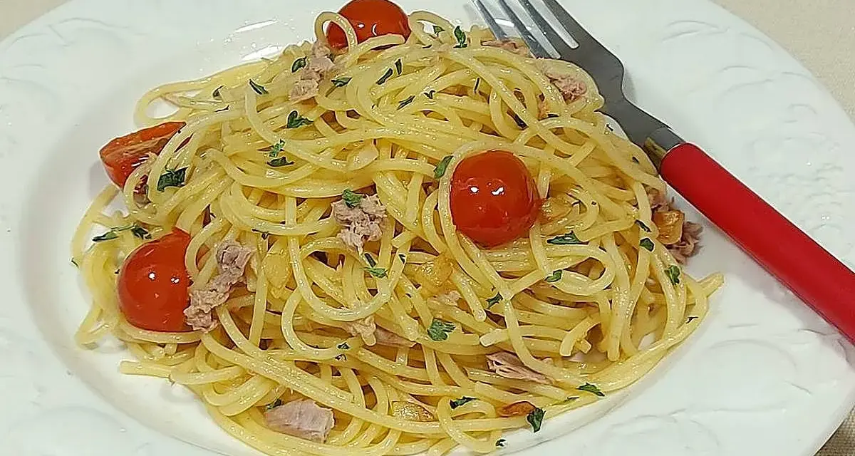 Espaguetis al ajillo con tomates cherry y atún, servidos en plato blanco con tenedor rojo.