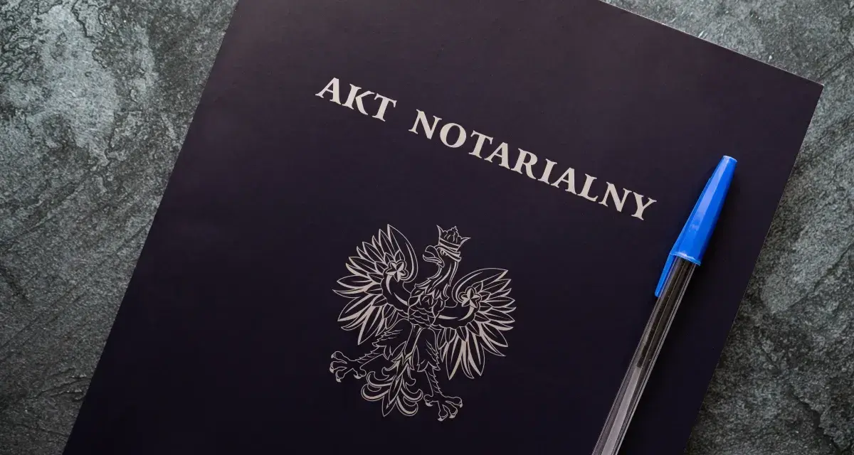 Na ciemnogranatowej okładce widnieje napis "AKT NOTARIALNY" i godło Polski. Obok leży niebieski długopis.