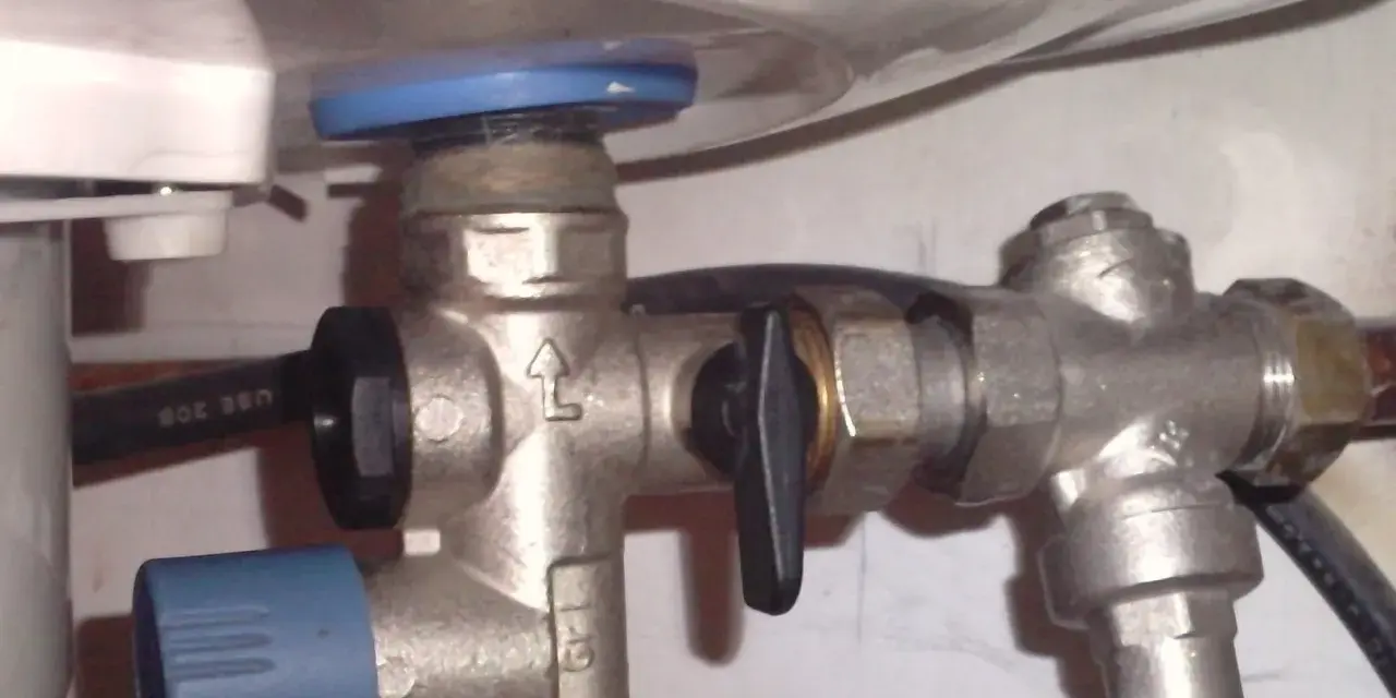 Un réducteur de pression, comme ce dispositif métallique avec une poignée noire, sert à réguler la pression de l'eau dans une installation.