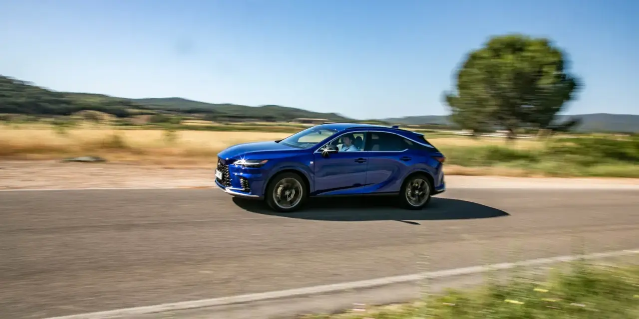 Niebieski Lexus 450h pędzi po wiejskiej drodze, otoczony zielenią i wzgórzami.