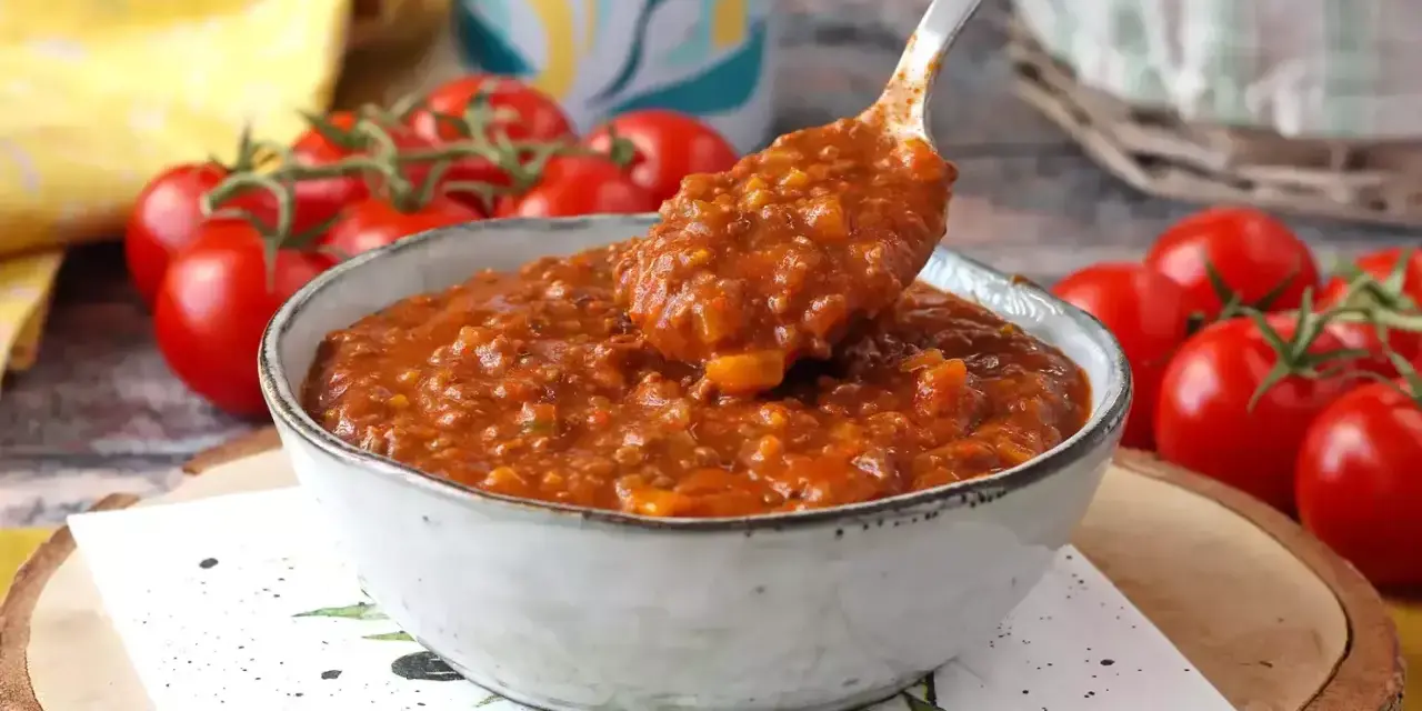 Gęsty, aromatyczny sos bolognese w misce, gotowy do podania. Obok świeże pomidory.
