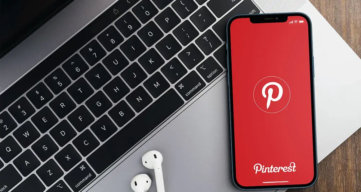 Telefon z aplikacją Pinterest obok klawiatury laptopa i słuchawek.