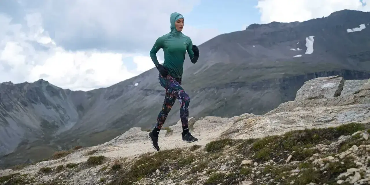 Kobieta w sportowym hidżabie biegnie po górskim szlaku, doskonaląc swoją kadencję w bieganiu.