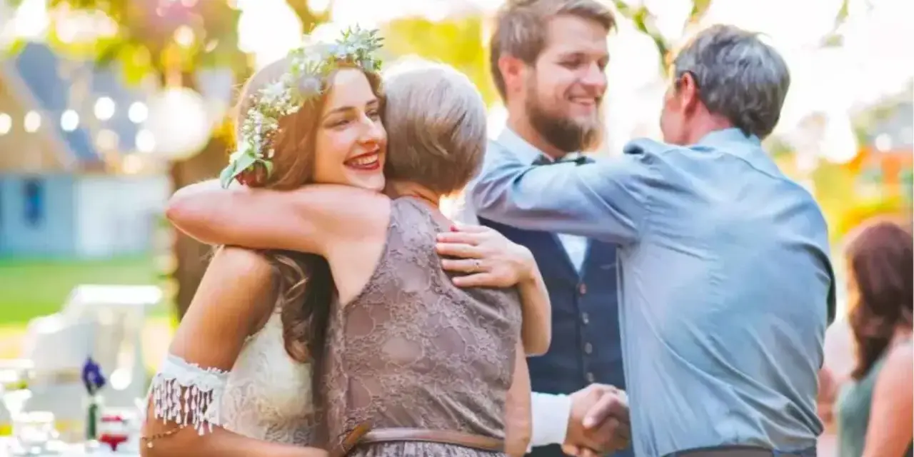 Uśmiechnięta panna młoda w wianku otrzymuje błogosławieństwo przed ślubem cywilnym od mamy. Narzeczony i ojciec obejmują się.