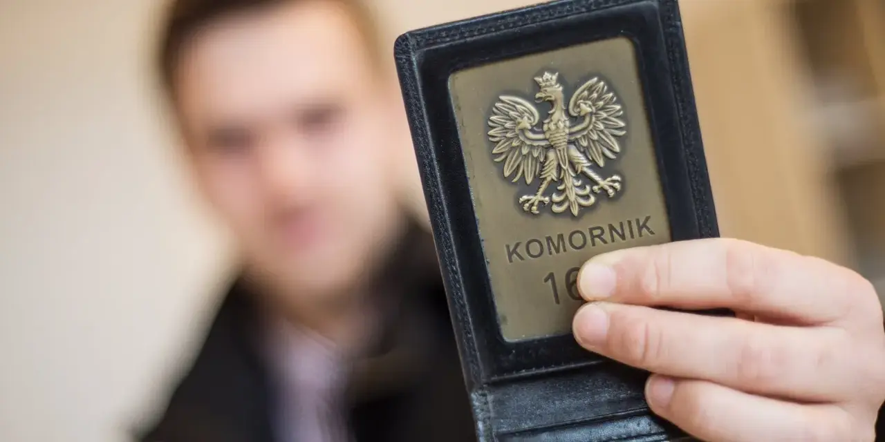 Komornik pokazuje legitymację z orłem. W tle niewyraźna postać mężczyzny, być może w związku z długiem osób prywatnych.