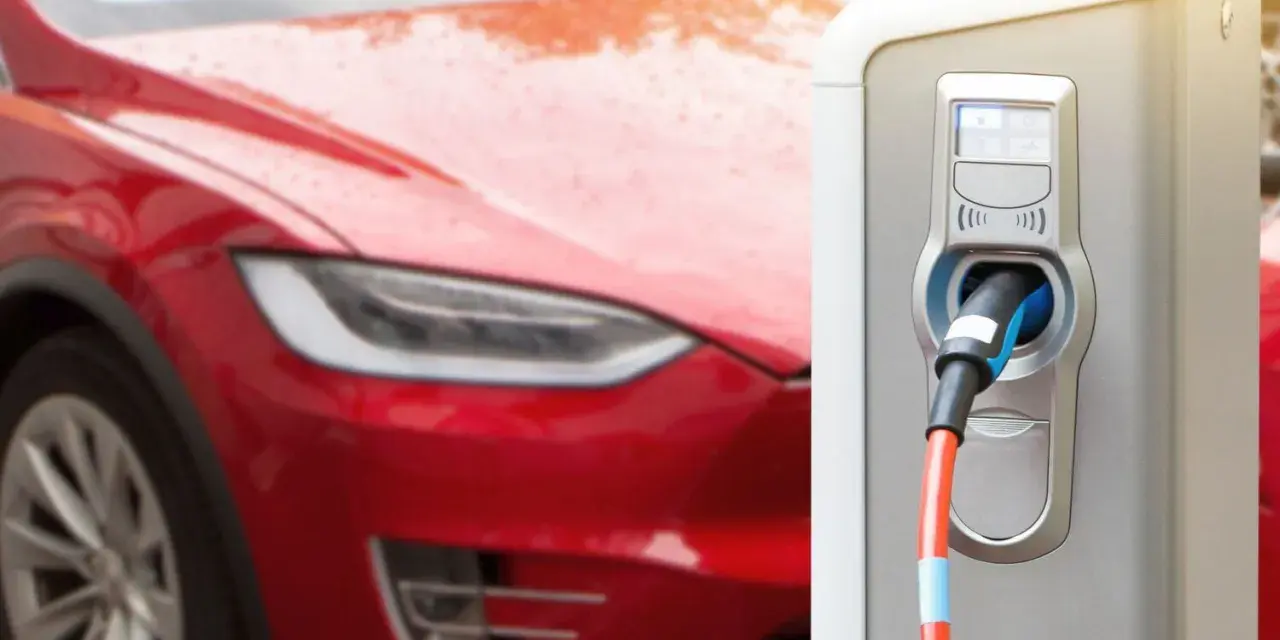 Czerwona Tesla podłączona do ładowarki elektrycznej.