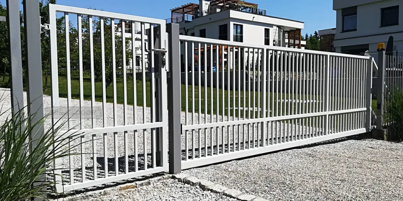 Brama z furtką bez słupka, otwarta na posesję z nowoczesnymi budynkami.