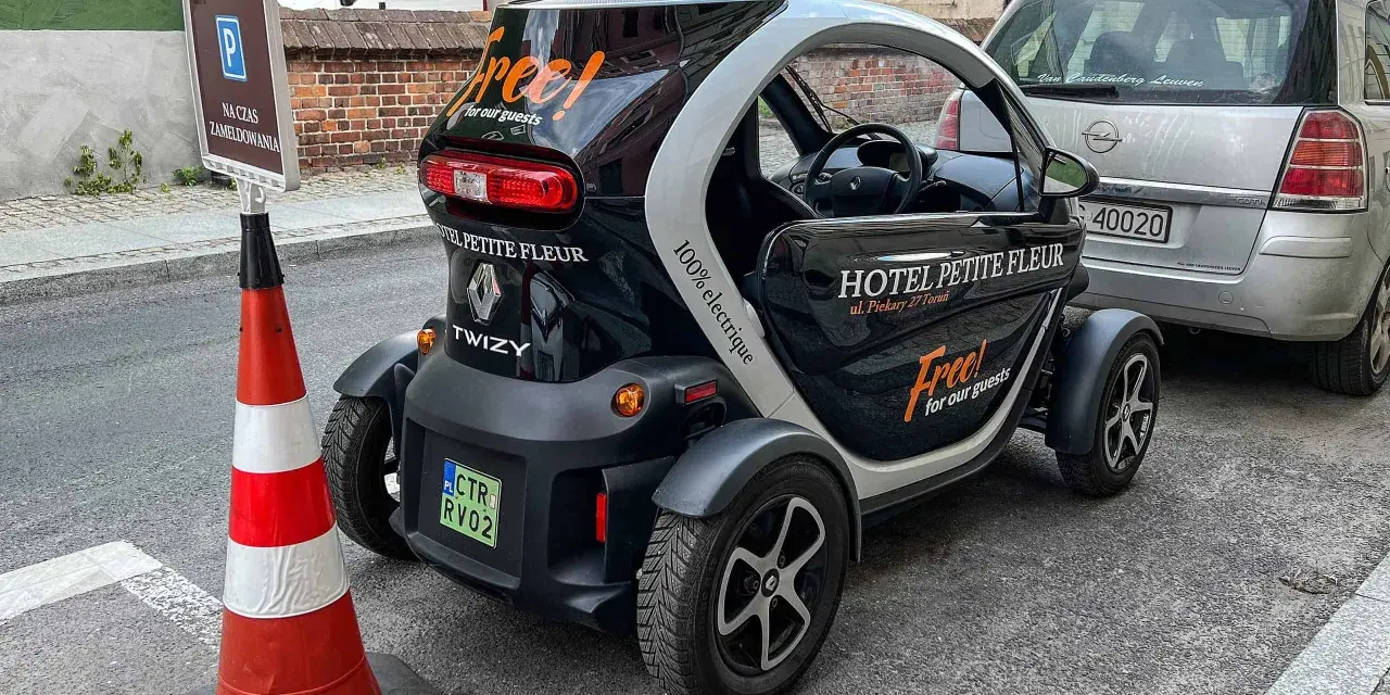 Czarny Renault Twizy z napisem "Free! for our guests" zaparkowany przed hotelem Petite Fleur. Obok znak parkingowy dla gości hotelowych.