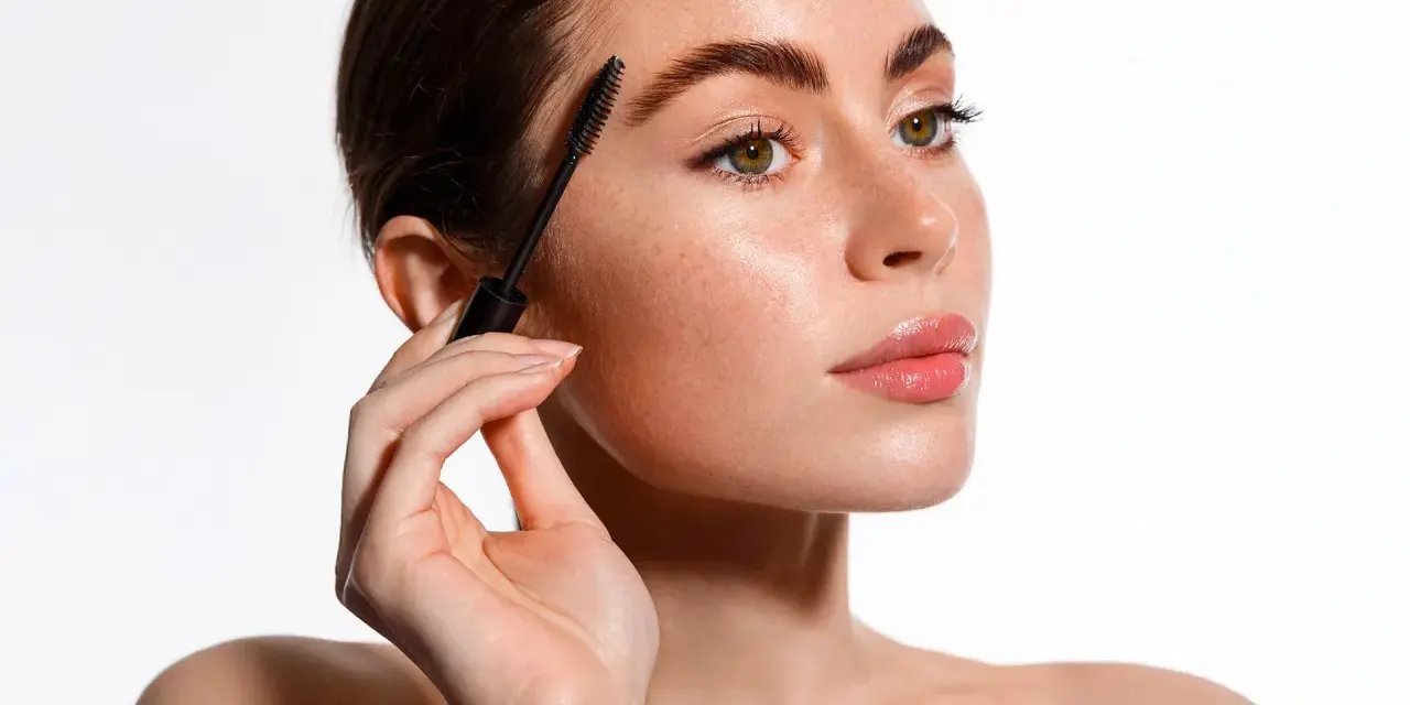 Une femme applique un mascara pour un maquillage des yeux parfait. Ses sourcils sont brossés et ses cils sont mis en valeur.