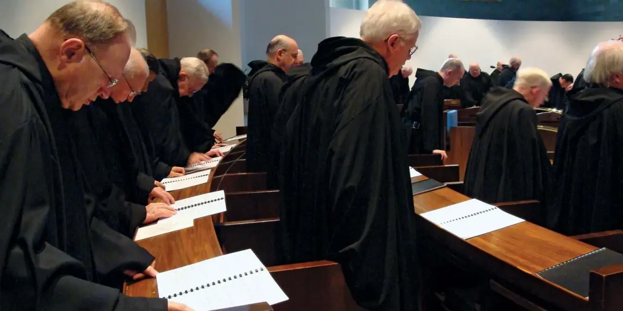 A group of Italian monks in black robes stand in a church, heads bowed over open prayer books.