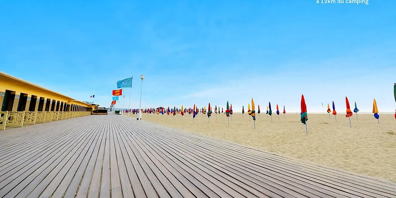 Plage de Deauville, parfaite pour une vacance scolaire en Normandie. Cabines colorées, parasols et ciel bleu azur.