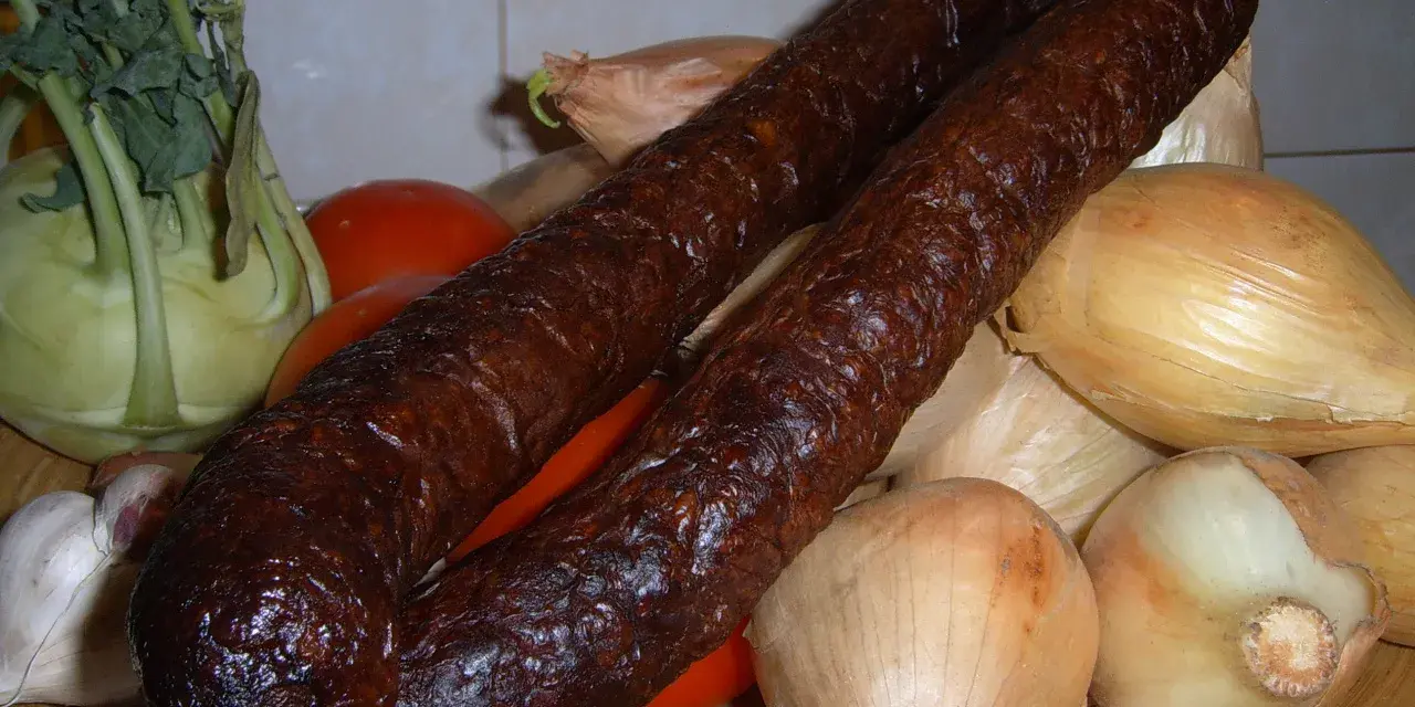 Wędzona kiełbasa z dzika na talerzu z warzywami: cebulą, pomidorami, kalarepą i czosnkiem.