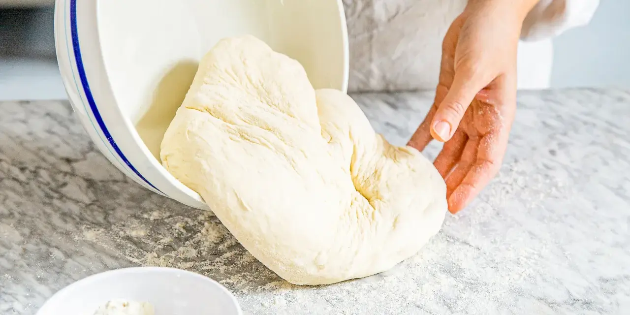 Frischer Teig, der aus einer Schüssel auf eine bemehlte Arbeitsfläche gleitet. Ähnlich wie Mehl Typ 0, ideal zum Backen.