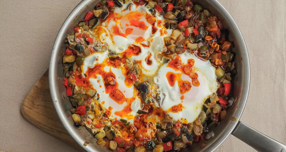 Huevos al plato con verduras salteadas, pimientos, calabacín y berenjena, todo en una sartén.