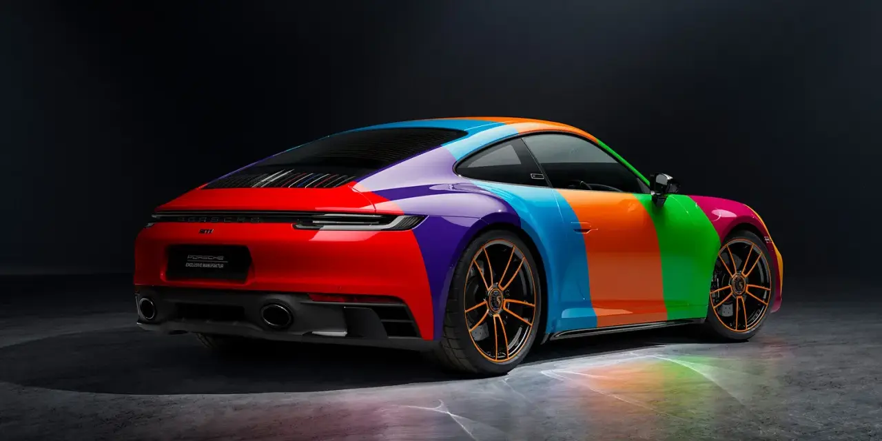 Porsche 911 Carrera GTS w tęczowym malowaniu, z pomarańczowymi felgami i odbiciami światła na podłożu.