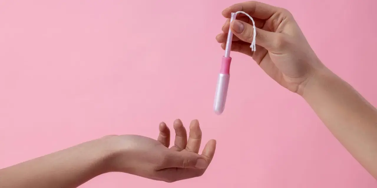 Dwie dłonie, jedna trzyma tampon z aplikatorem, druga wyciągnięta do przyjęcia. Ciasna pochwa to temat, który wymaga dyskrecji.