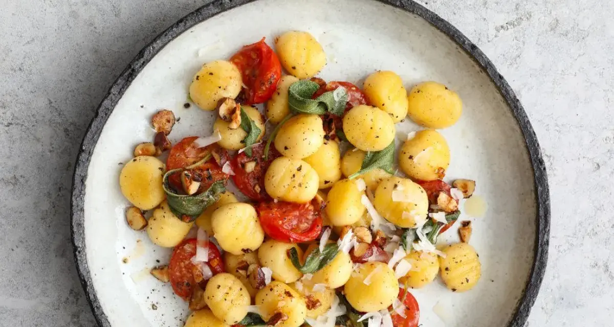 Gnocchi z pomidorkami koktajlowymi, szałwią i orzechami laskowymi, posypane parmezanem. Pyszne danie na obiad.