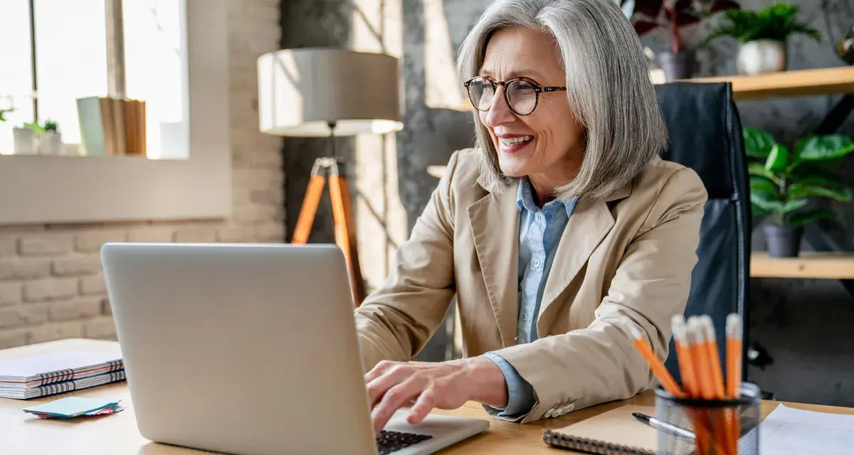 Femme souriante travaillant sur son ordinateur portable, planifiant sa future pension pré cheval.