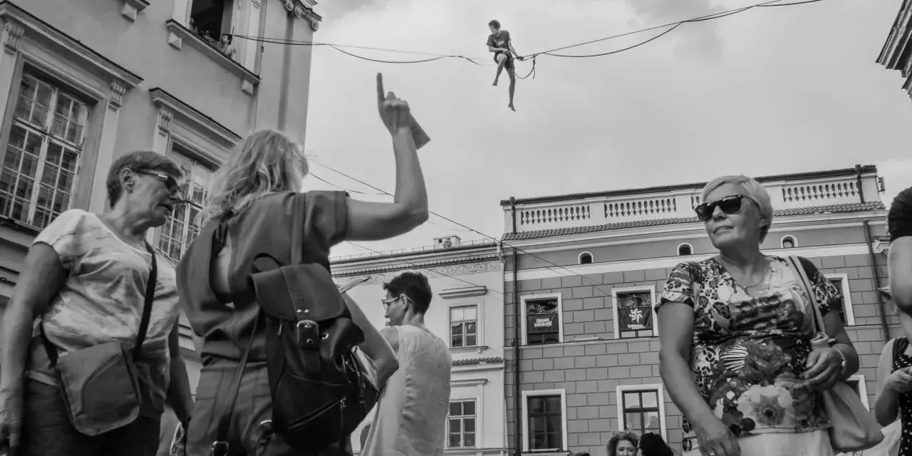 Street foto: tłum na ulicy obserwuje śmiałka balansującego na linie.
