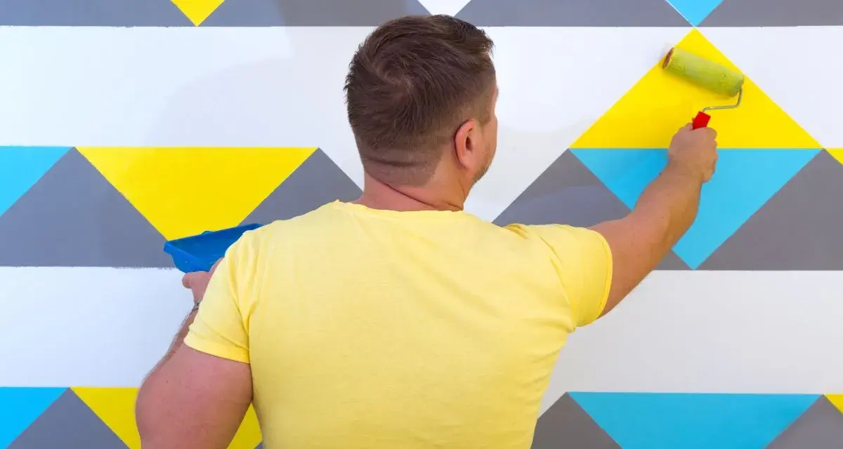 Un homme peint un mur avec un rouleau, créant un modèle de peinture géométrique aux couleurs vives.
