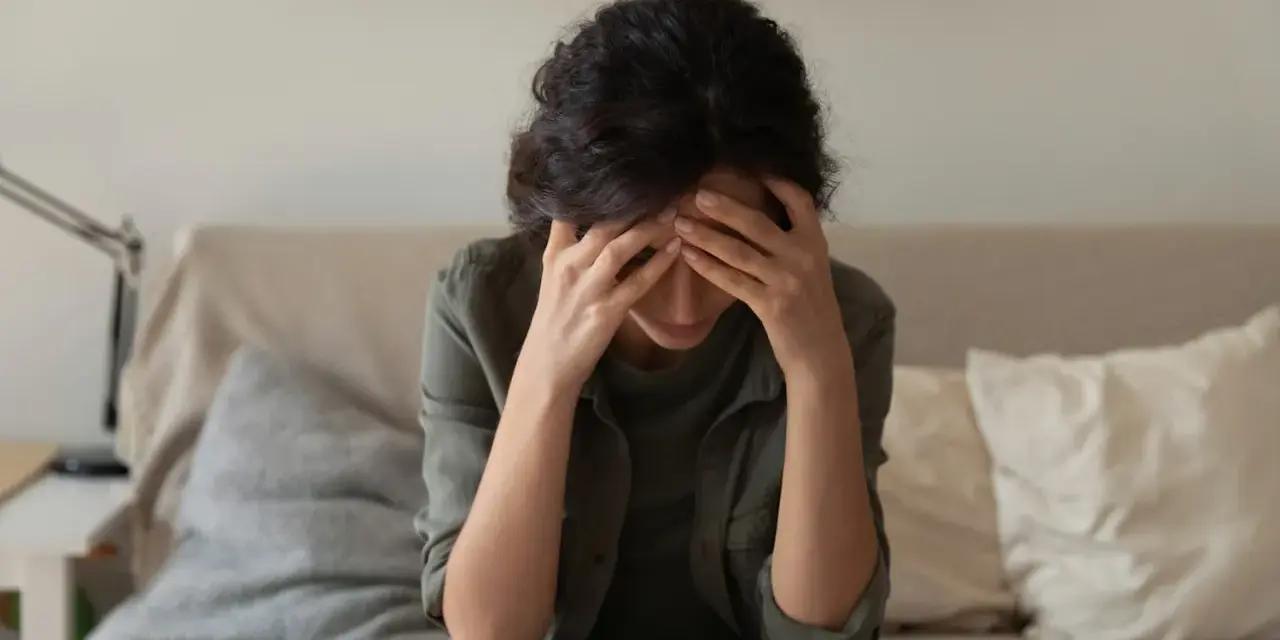 A woman sits with her head in her hands, overwhelmed by the cycle of self-destruction.