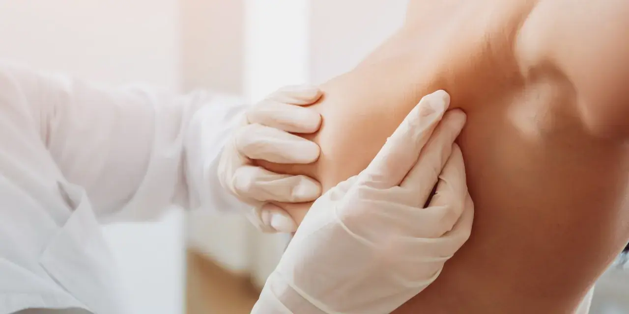 Arzt in Handschuhen tastet Brust ab.