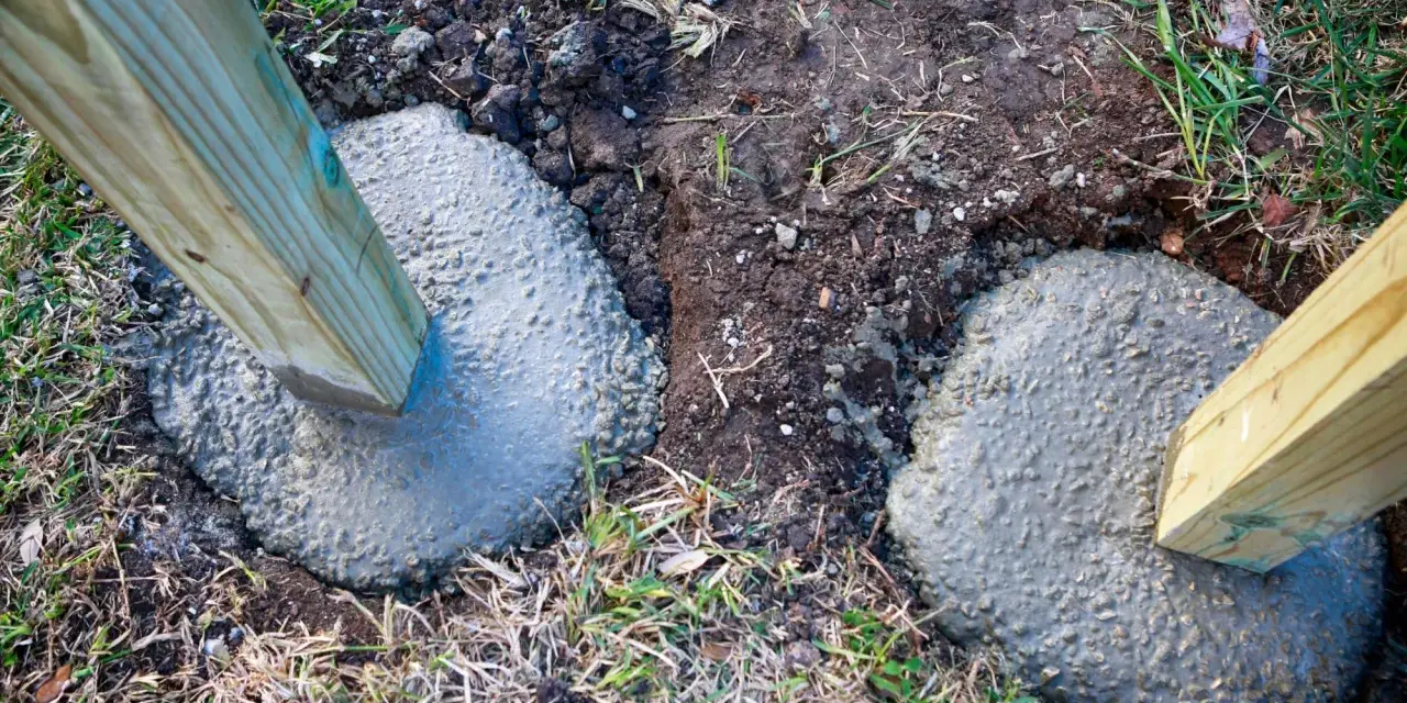 Holzpfosten werden in frisch gegossenen Beton gesetzt, um einen stabilen Zaun zu bauen. Das Einbetonieren der Zaunpfosten sorgt für Langlebigkeit.