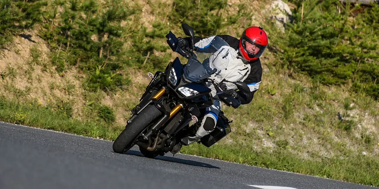 Motocyklista w kasku na zakręcie górskiej drogi. Planujesz podróż na Korsykę? Sprawdź ceny paliwa i noclegów!