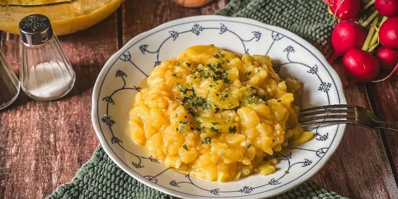 Omas Kartoffelsalat, ein Klassiker auf dem Holztisch, garniert mit Petersilie. Daneben Radieschen und Salzstreuer.