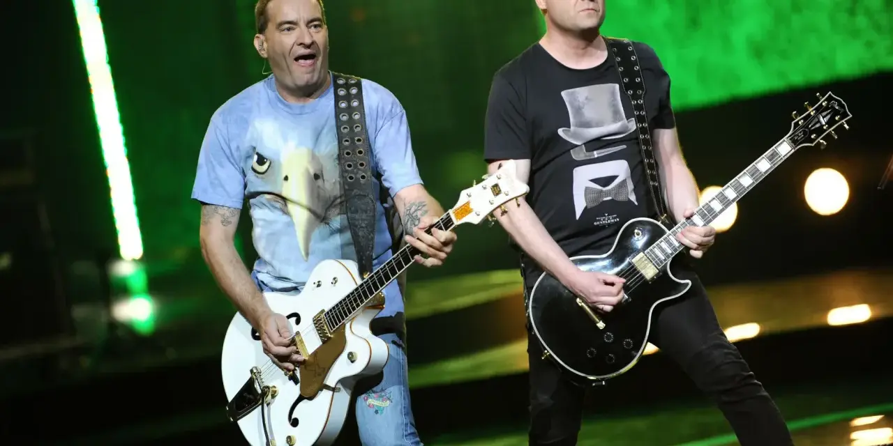 Dwóch członków Kobranocki gra na gitarach podczas koncertu. Jeden w koszulce z orłem, drugi w czarnej z cylindrem i muszką.