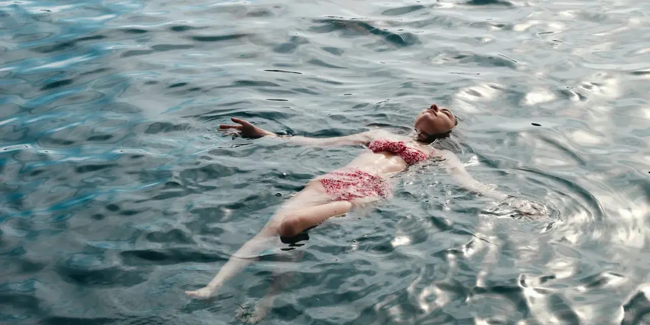 Une femme flotte paisiblement sur l'eau, profitant des ampoules eau de mer bienfaits pour la relaxation et le bien-être.