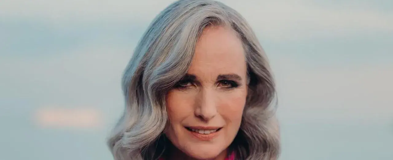 Mujer de 50 años con cabello plateado y ondulado, sonriendo suavemente. Se aprecian las líneas de expresión, reflejo de la flacidez facial a los 50.