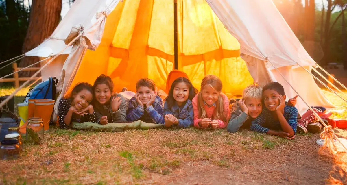Sept enfants souriants allongés devant une tente de camping éclairée par le soleil.