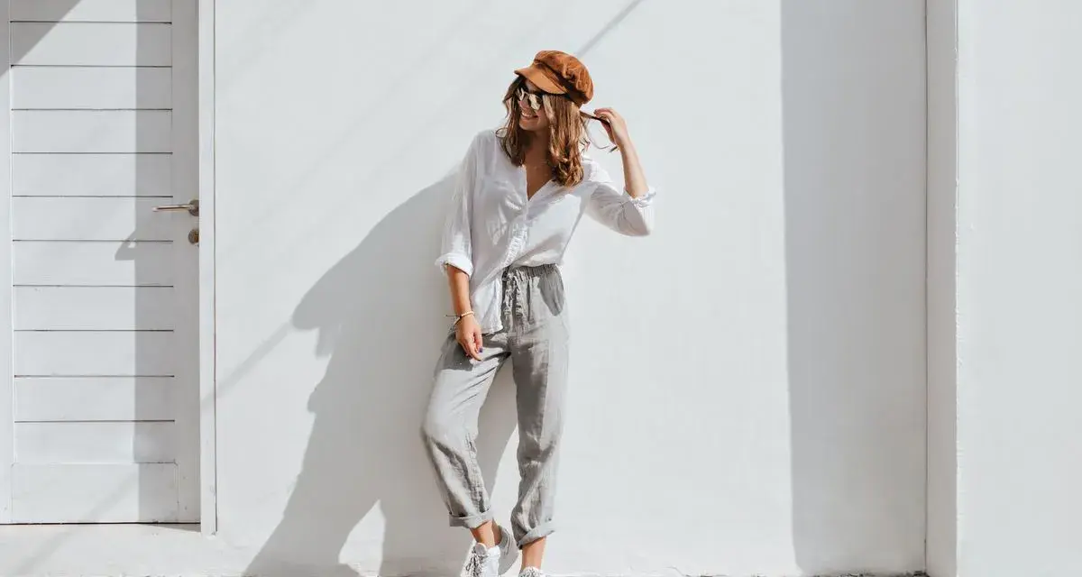 Modello con cappello marrone e occhiali da sole, indossa una camicia bianca e pantaloni grigi. Un esempio di abbinamenti outfit grigio casual e chic.