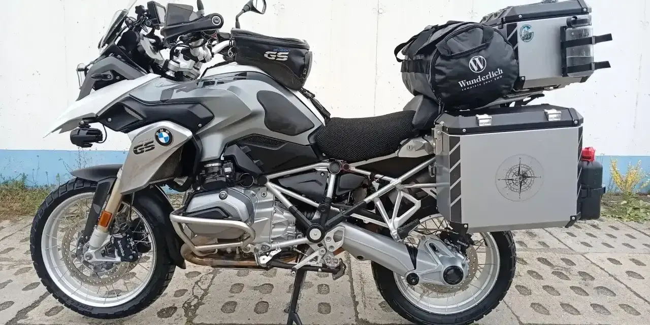 Srebrny motocykl BMW R1200GS z kuframi i torbą na bak. Wady tego modelu to m.in. wysoka cena i skomplikowana elektronika.
