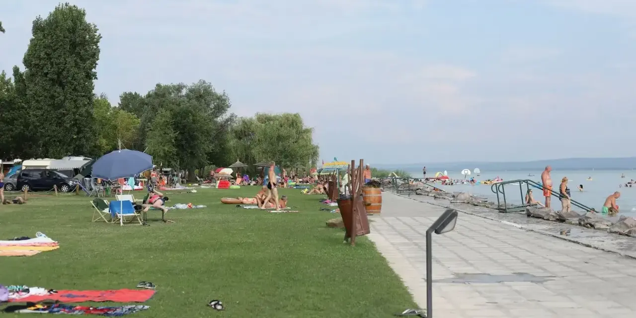 Ludzie odpoczywają na plaży i w wodzie. W tle widać kampery, co sugeruje, że to popularne miejsce na napfeny camping.