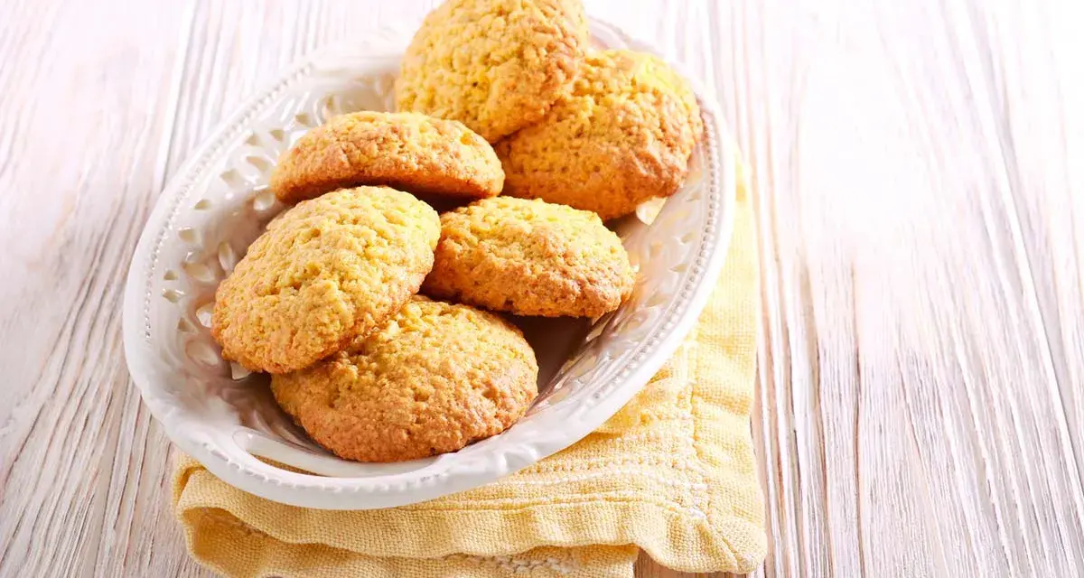 Biscotti con farina di mais dorati e friabili, serviti in un piatto bianco su un tovagliolo giallo.