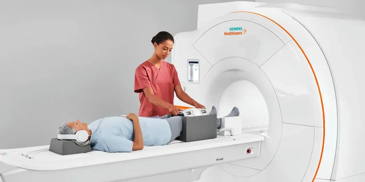 Pacjent leży na łóżku rezonansu magnetycznego, a technik przygotowuje jego nogi do badania. To właśnie mri co to za badanie, które pozwala zajrzeć do wnętrza ciała.