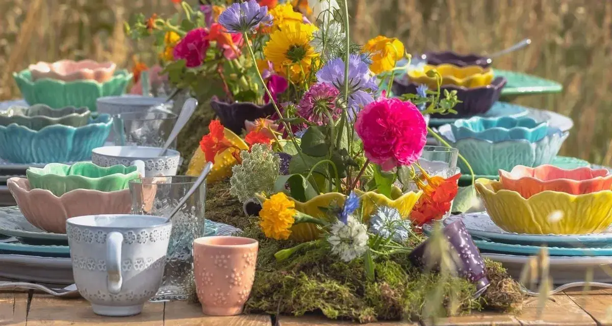 Färgglada uppläggningsfat i plast, staplade med blommor och glas, skapar en festlig dukning utomhus.
