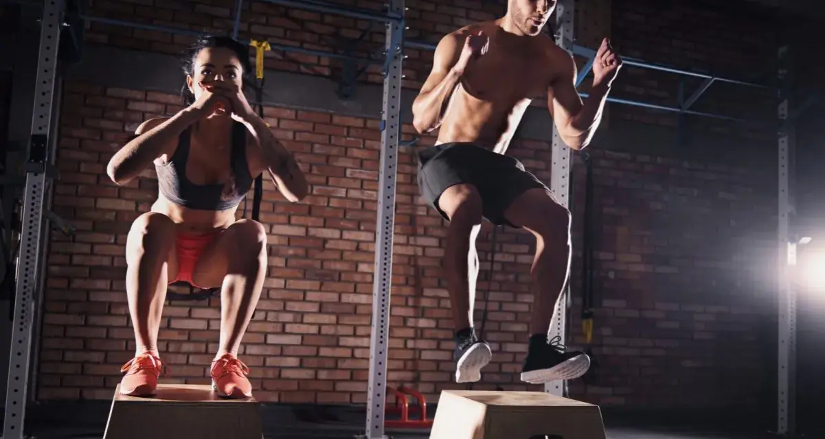 Para ćwicząca CrossFit wykonuje skoki na skrzyni w siłowni.