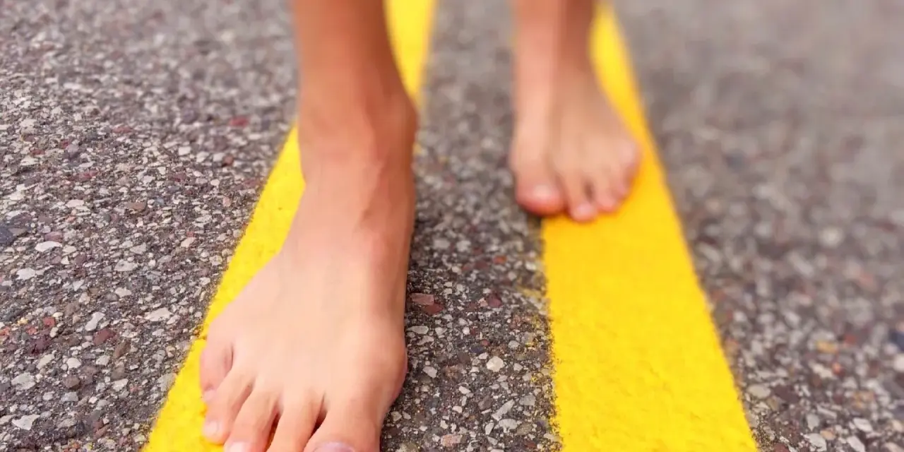 Piedi nudi che camminano su una strada con strisce gialle. Un'esperienza di correre scalzi per sentire la strada.