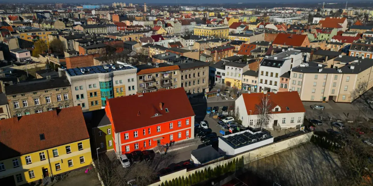 Widok z lotu ptaka na miasto, gdzie leży Ostrów Wielkopolski. Widać kolorowe kamienice, dachy i samochody.