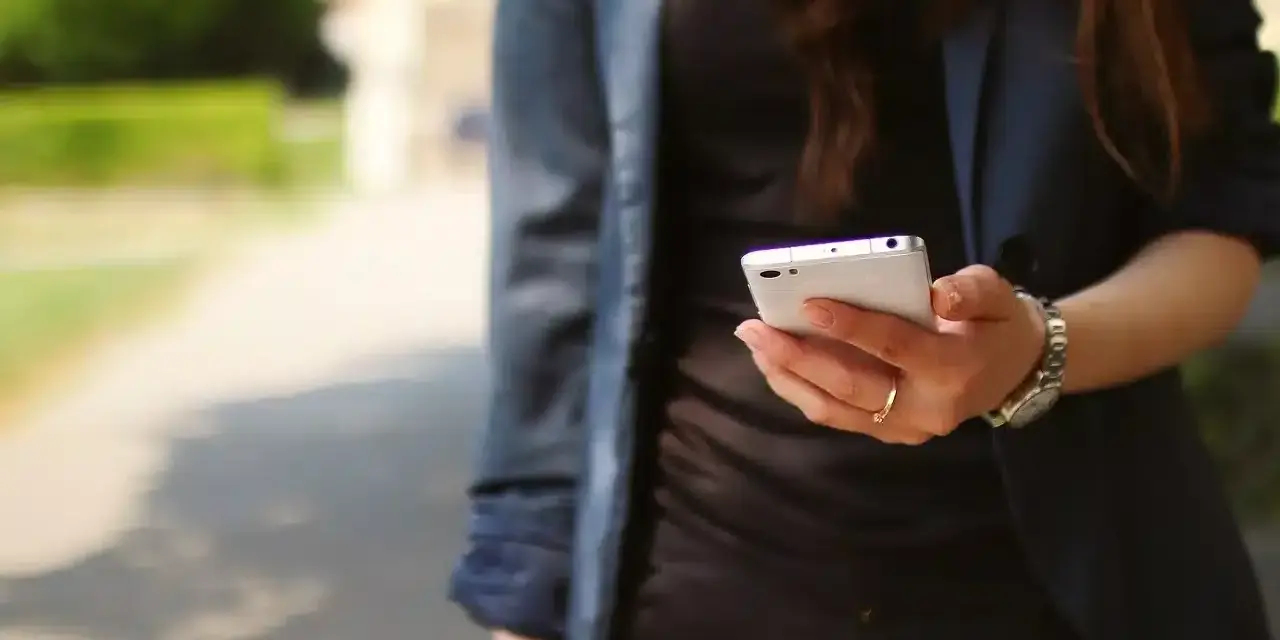 Kobieta z telefonem w dłoni, być może szuka przykładów uporczywego nękania w internecie.