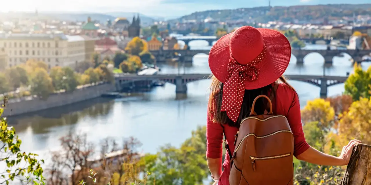 Donna con cappello rosso ammira Praga in autunno. Il periodo migliore per andare a Praga è quando la natura si tinge di colori caldi.